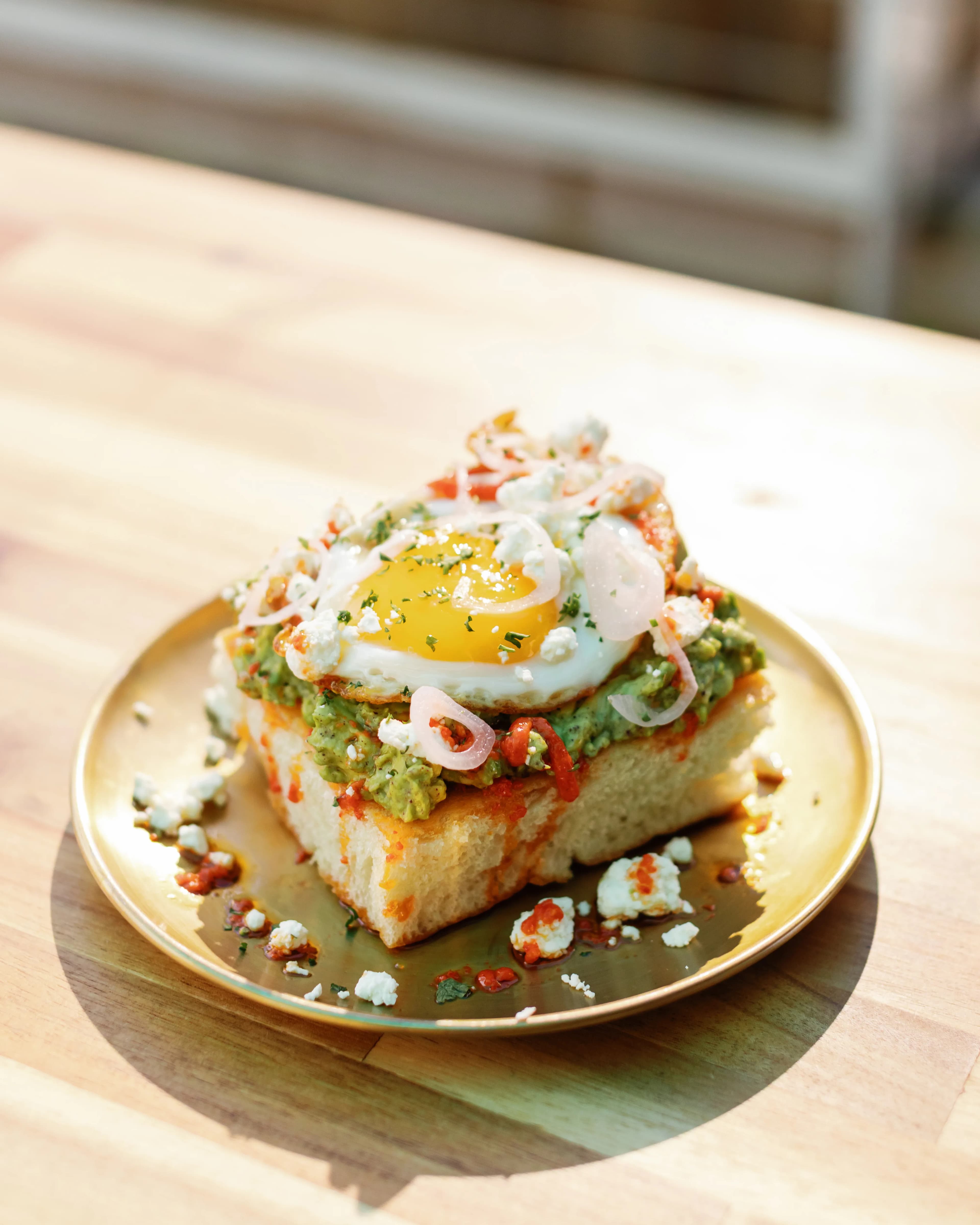Darling Aviary avocado toast with fried egg, crumbled feta and pickled shallots on a gold plate — farm-to-fork rooftop kitchen at 712 K Street in DoCo, Downtown Sacramento