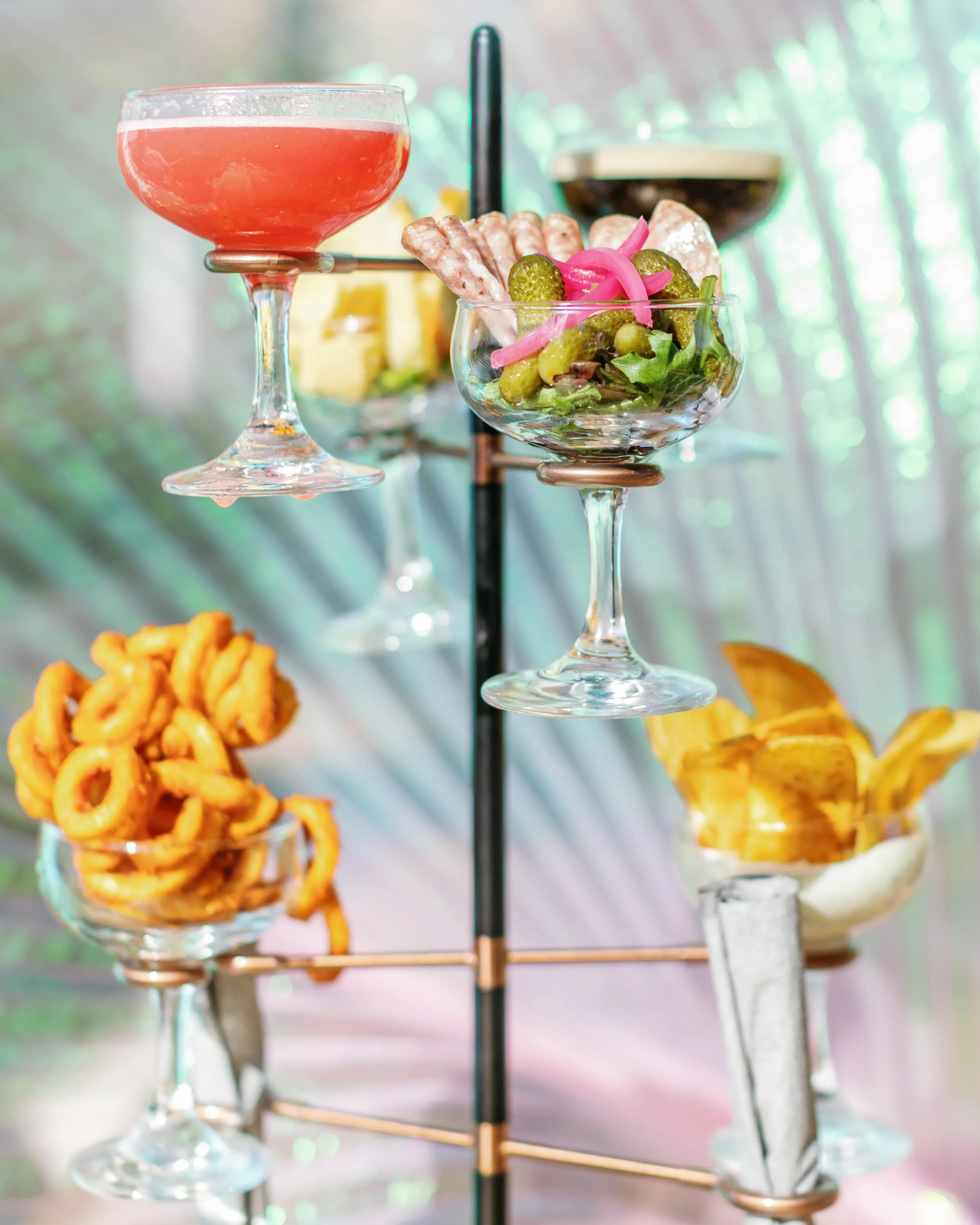 Darling Aviary happy hour cocktail snack tower with pink strawberry coupe cocktail, charcuterie, olives, curly fries and golden chips — rooftop bar in Downtown Sacramento, Mon–Fri 4–7 PM