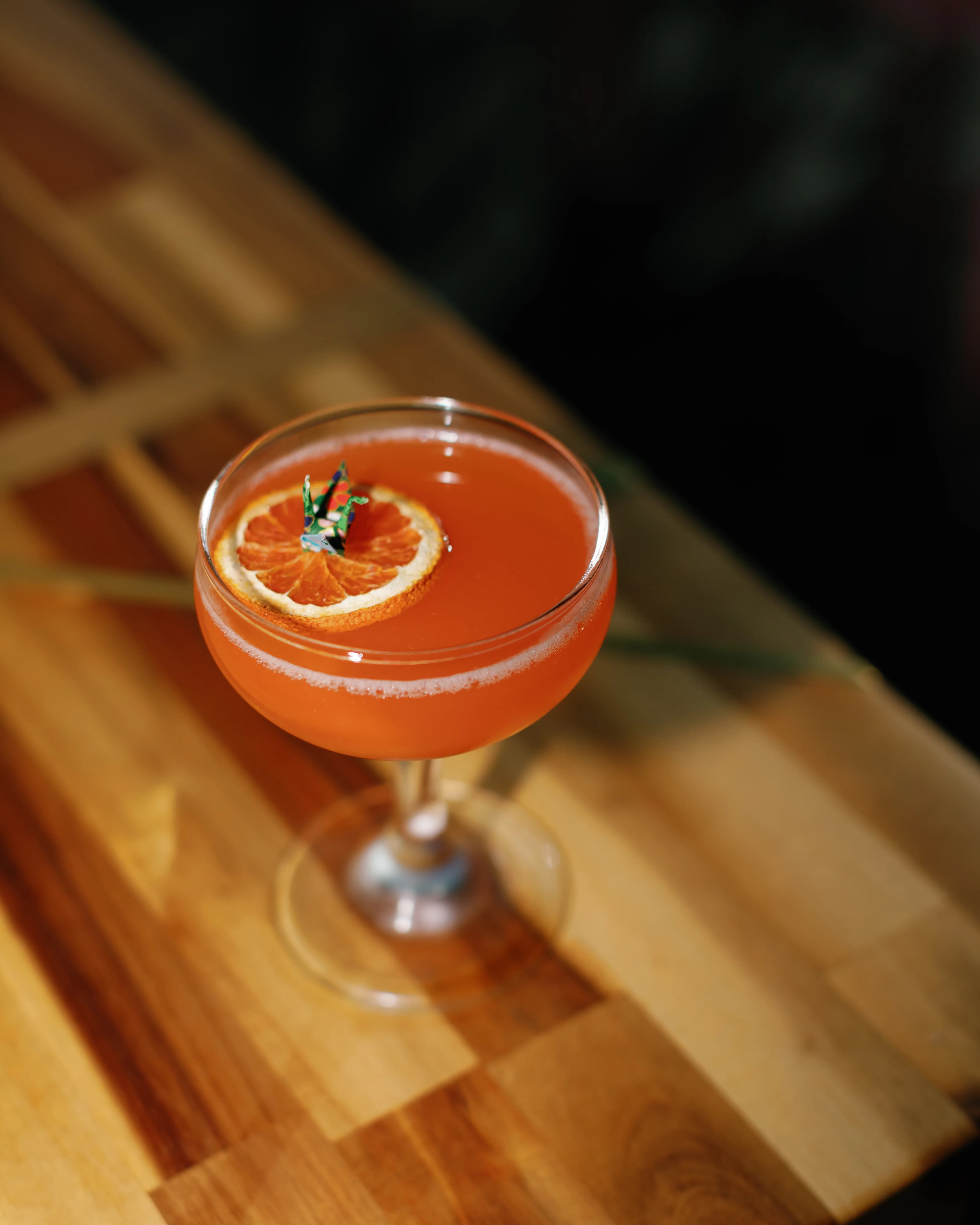 Darling Aviary Paper Plane cocktail in a coupe glass with marigold and fresh orange garnish — handcrafted rooftop bar program at DoCo, Downtown Sacramento