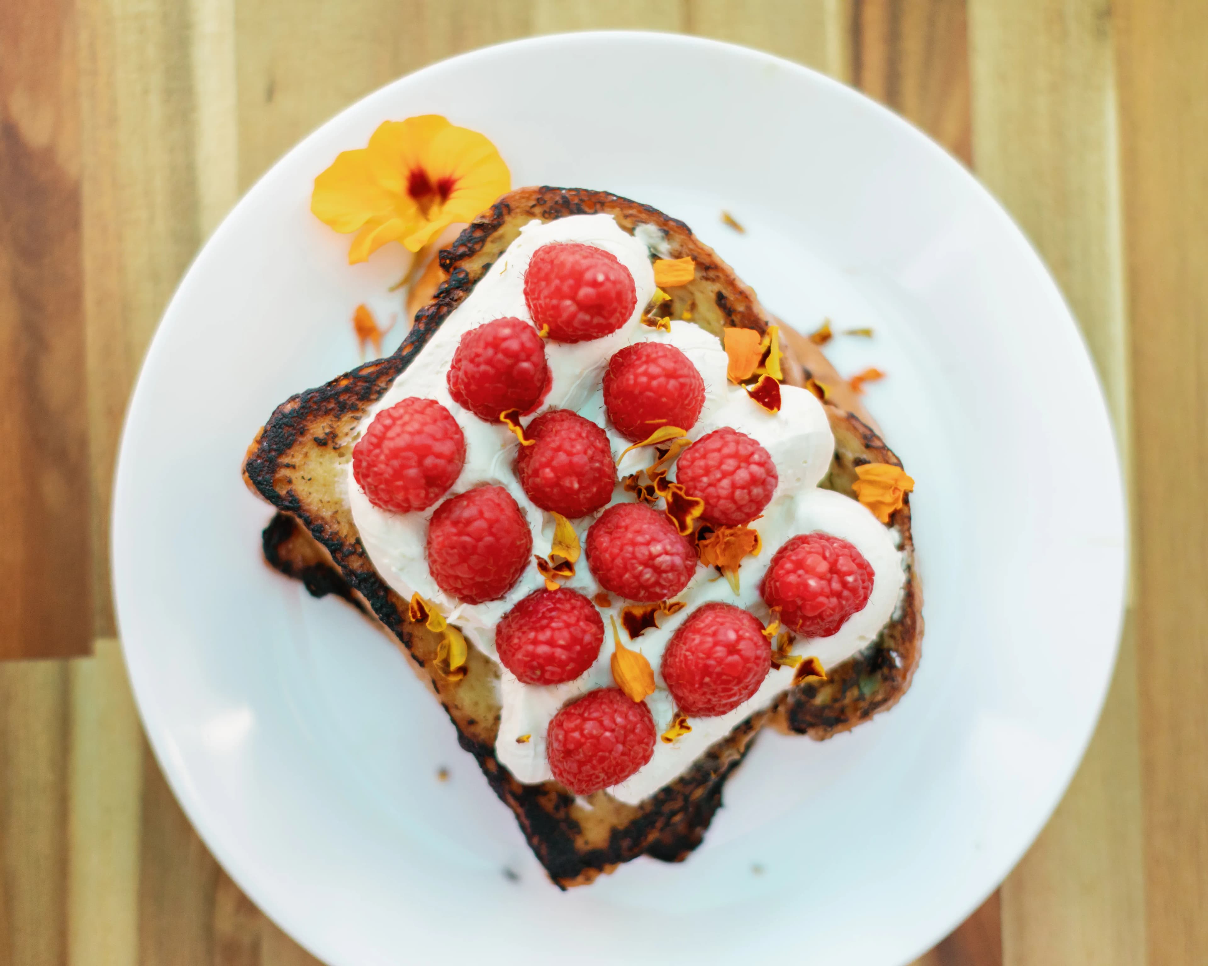 Overhead view of Darling Aviary raspberry French toast with whipped cream, fresh raspberries and a nasturtium flower — weekend rooftop brunch in Downtown Sacramento, Sat & Sun from 11 AM