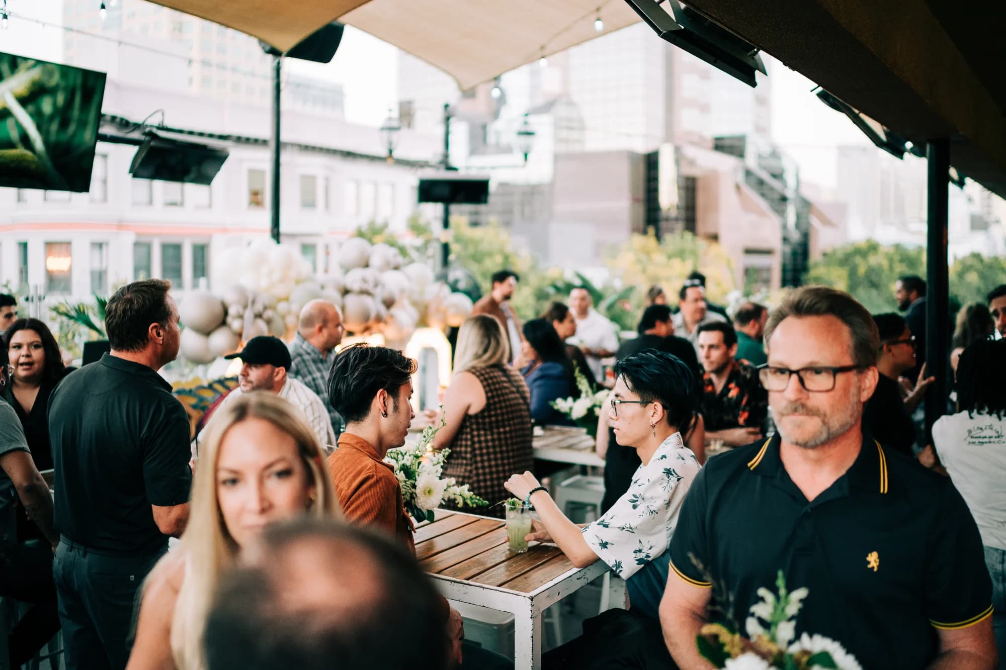 Guests mingling at a private rooftop event at Darling Aviary with cocktails, patio tables and a view of K Street in Downtown Sacramento at golden hour