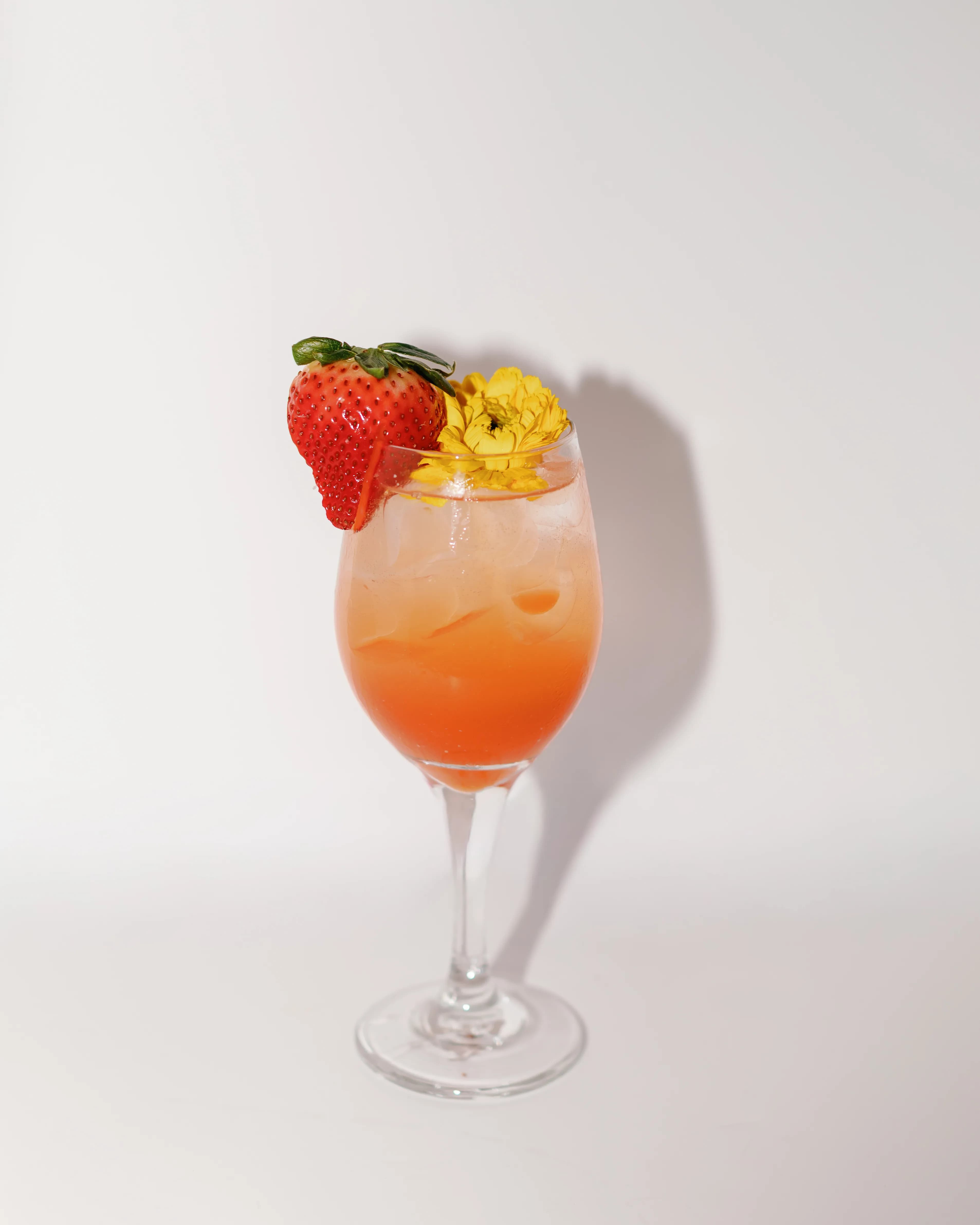 Darling Aviary Strawberry Blossom cocktail in a wine glass with a peach-to-orange gradient, fresh strawberry and yellow edible flower garnish at rooftop bar in DoCo, Downtown Sacramento